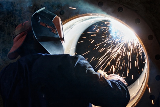 A metalworker welding a metal barrel